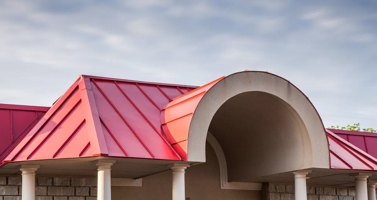 Red standing-seam metal roof on a commercial building with a domed entry.