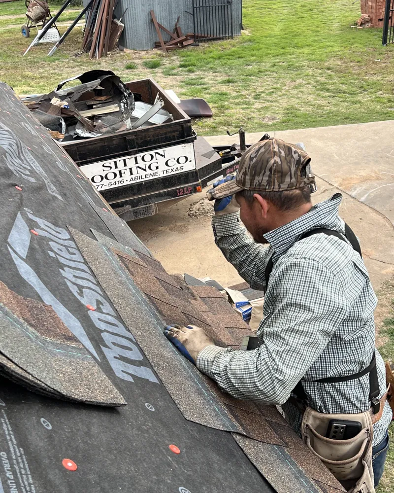 Roofer laying shingles next to a Sitton Roofing Co. trailer.