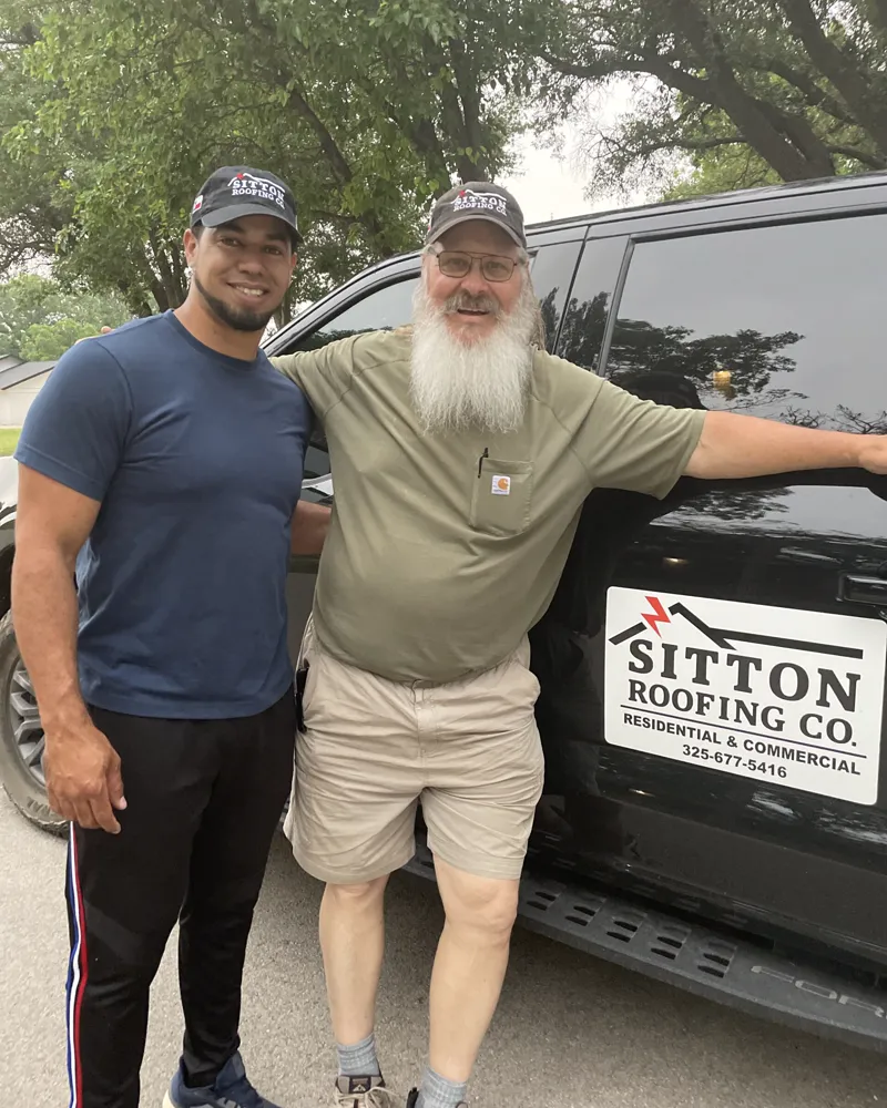 Two men standing by a pickup with a Sitton Roofing Co. sign on the door.